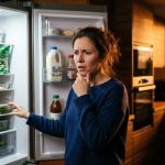 Femme devant son réfrigérateur se demandant quoi manger après un diagnostic de diabète, de cholestérol élevé ou d'hypertension.